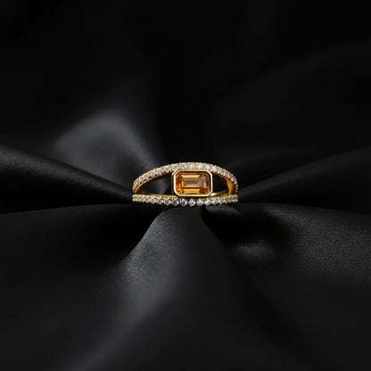 Gold ring with a central orange gemstone and diamond accents on a white background